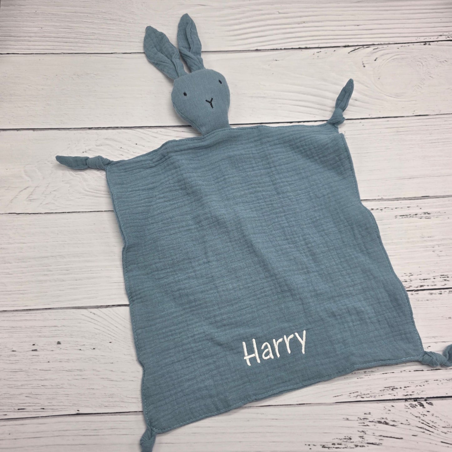 Blue textured blanket with a bunny toy and 'Harry' embroidered on a wooden surface