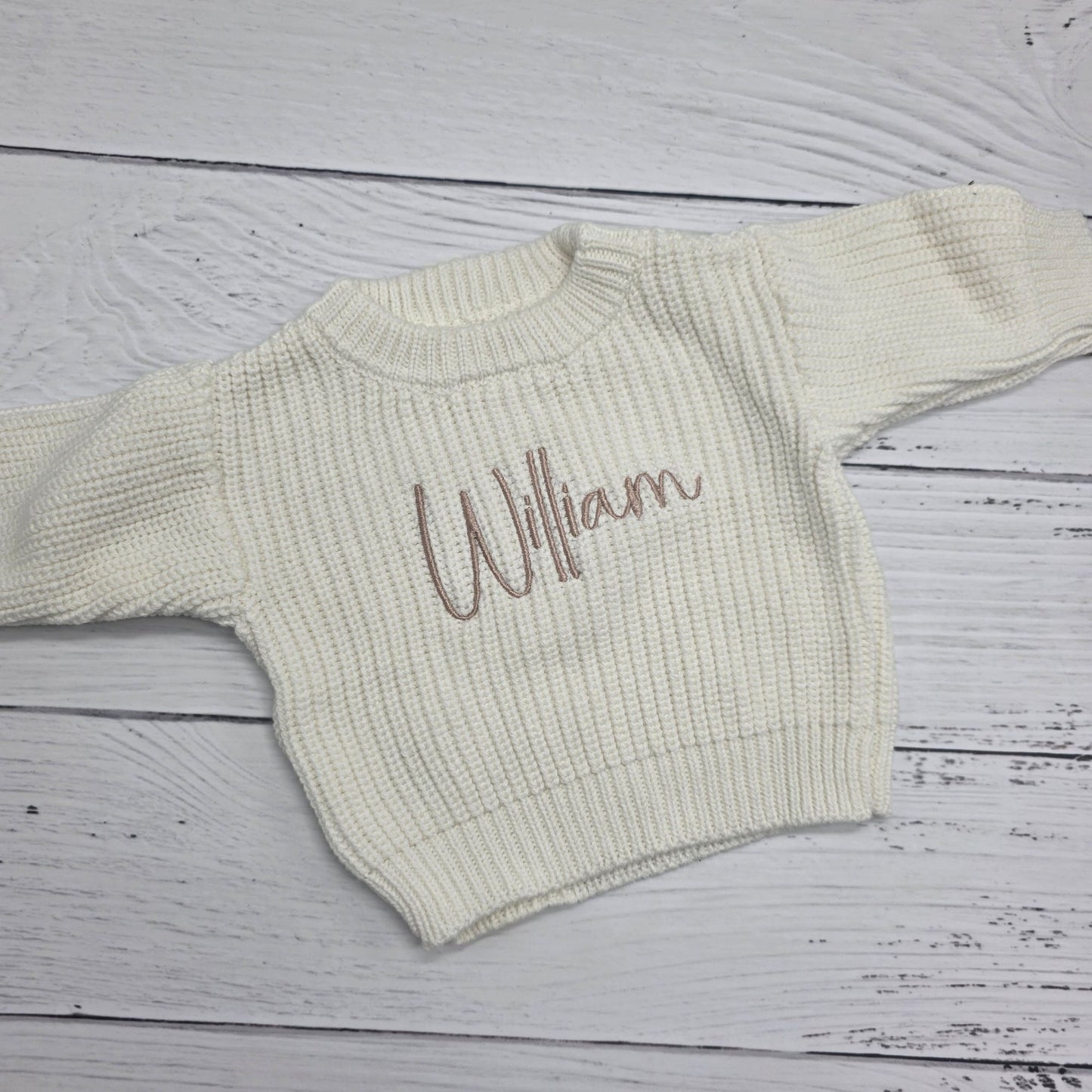 Cream-colored sweater with 'William' embroidered on a wooden surface