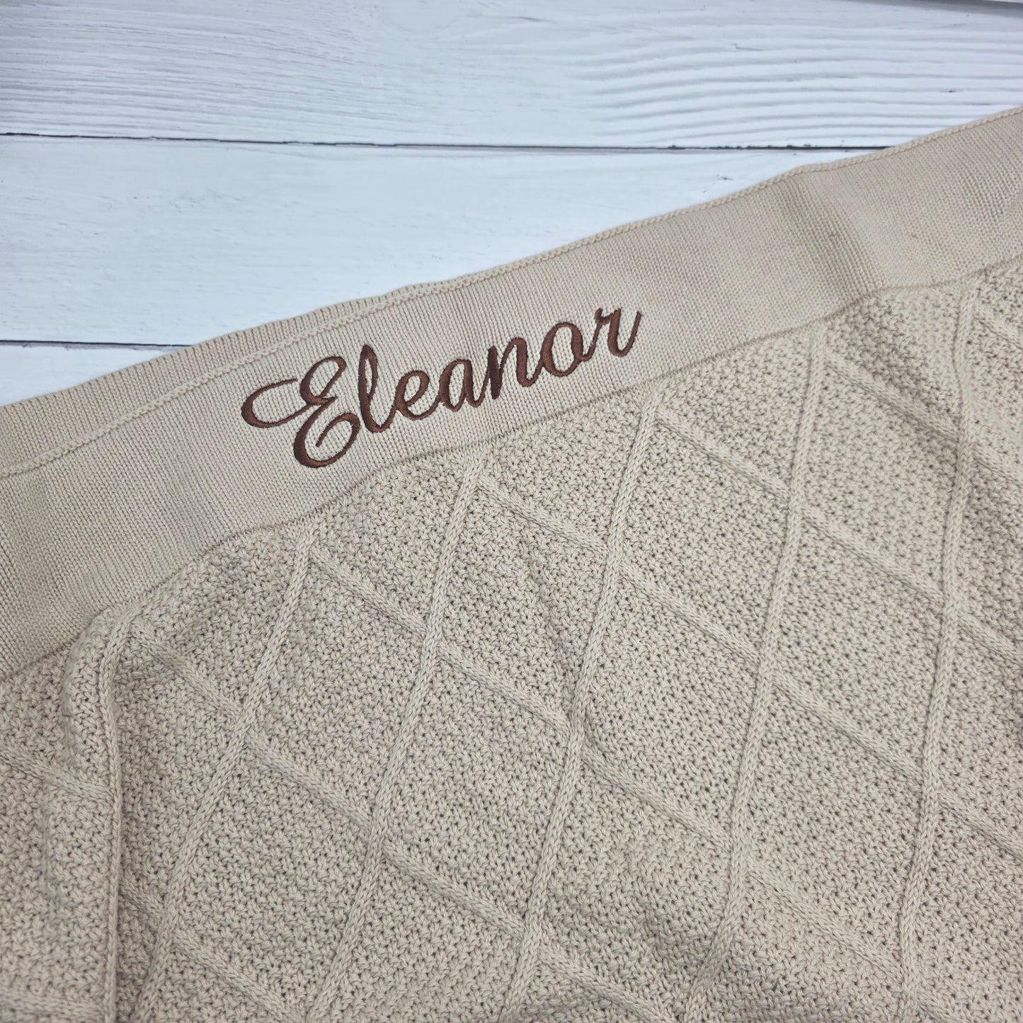 Textured beige fabric with embroidered name 'Eleanor' on a light wooden surface