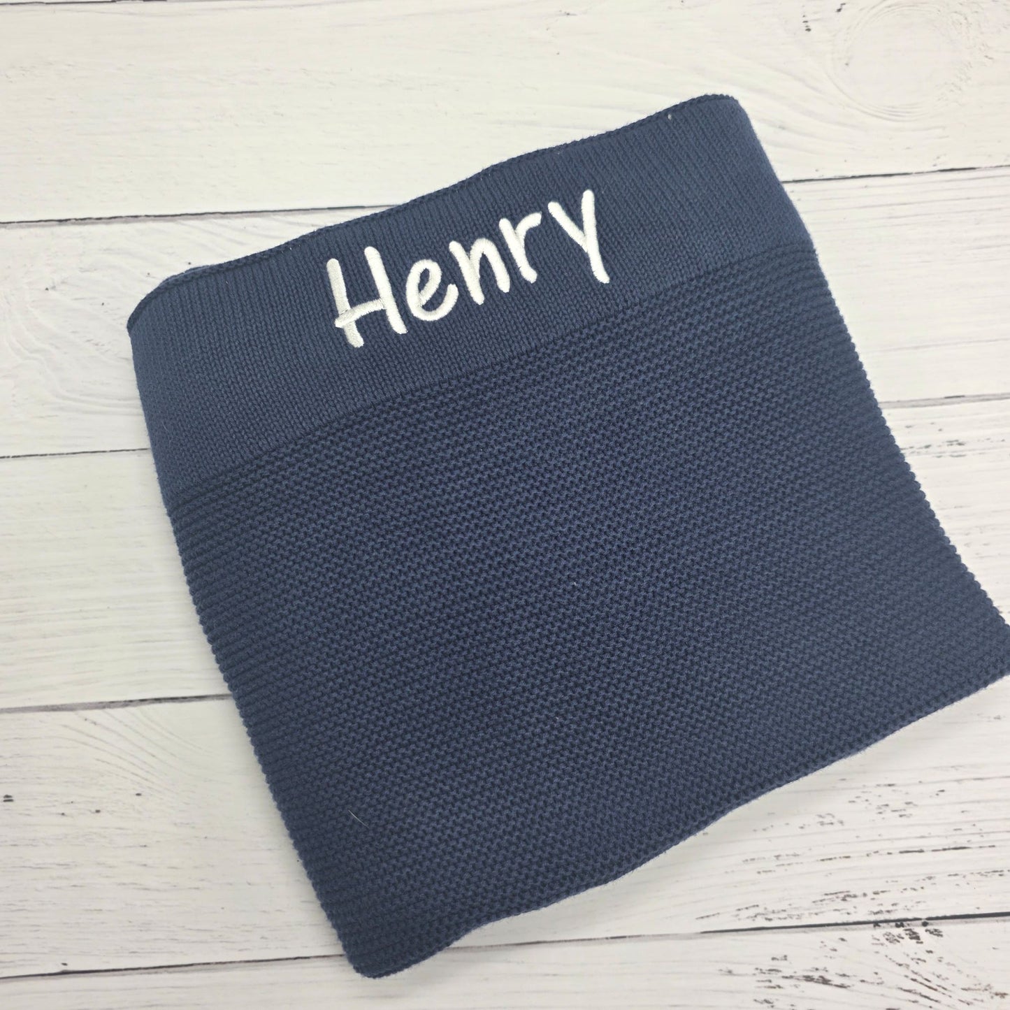 Navy blue knitted blanket with 'Henry' embroidered on a light wooden surface