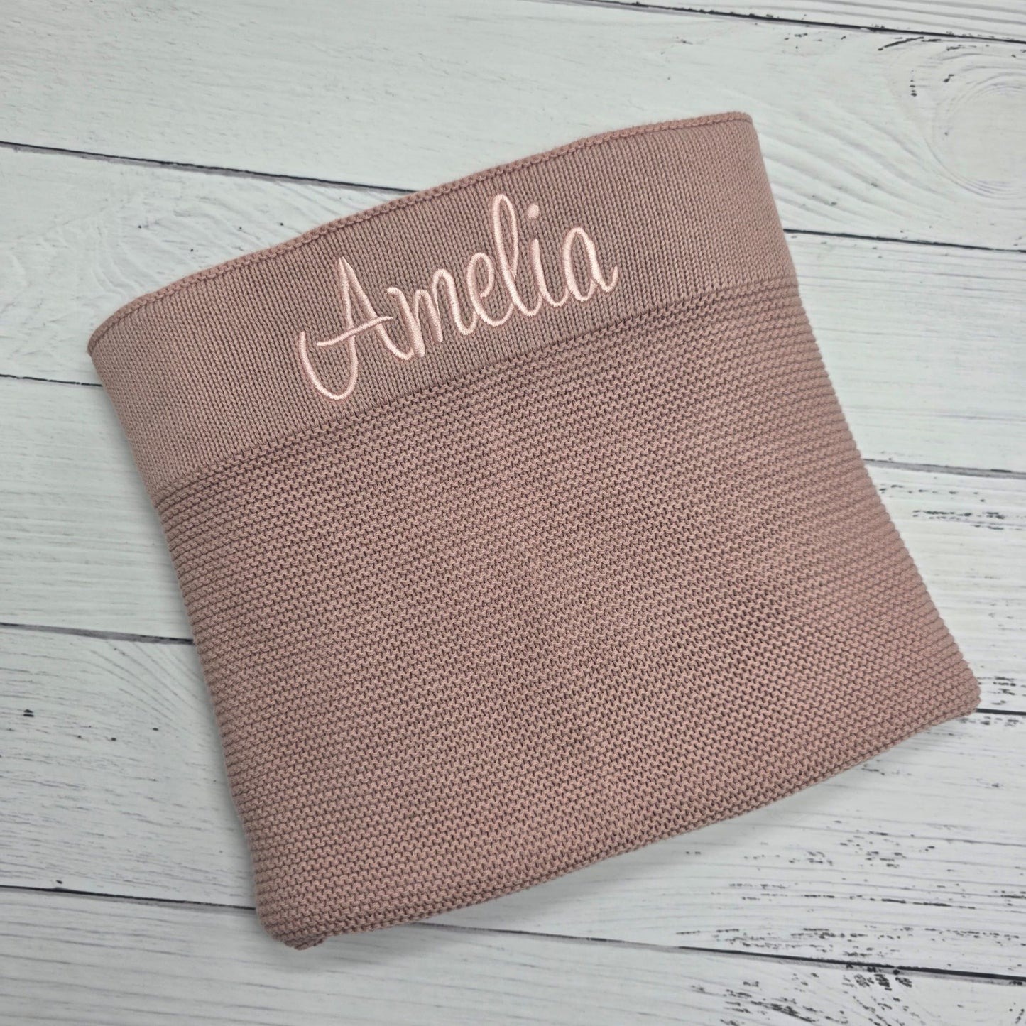 Pink woven blanket with 'Amelia' embroidery on a wooden surface