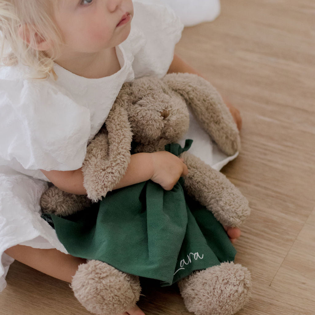 Child holding a nana huchy christmas bunny wearing a green dress with personalised name embroidered on it.