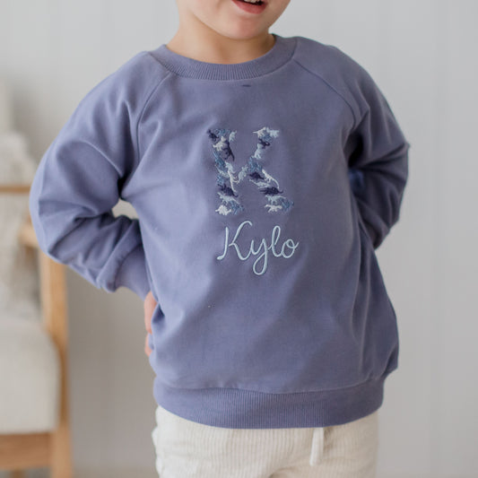 blue baby and toddler crewneck embroidered with a dinosaur name design using a blue colour theme