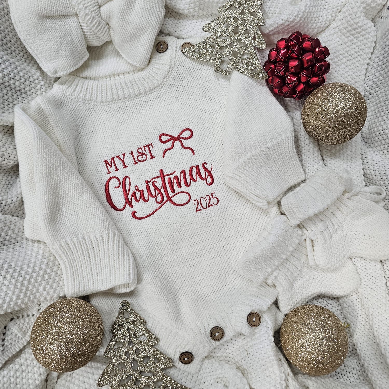 Baby onesie with 'My 1st Christmas 2025' text, surrounded by festive decorations on a textured surface.