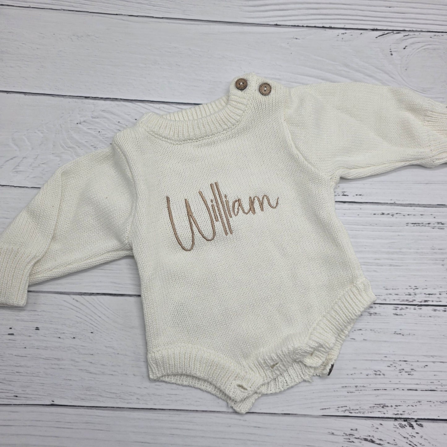 Baby romper with 'William' printed on it, laid flat on a wooden surface