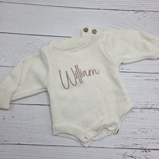 Baby romper with 'William' printed on it, laid flat on a wooden surface