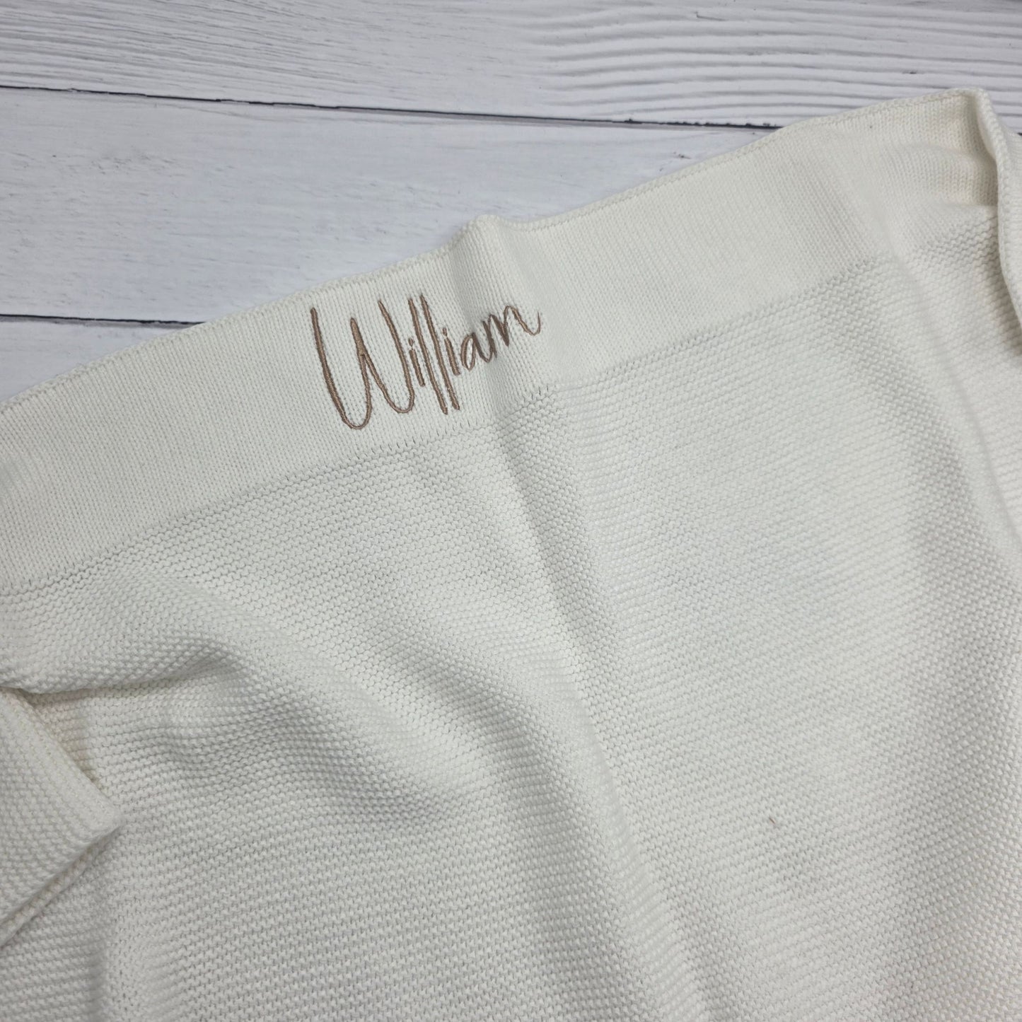 Light gray fabric with 'William' embroidered on a wooden surface