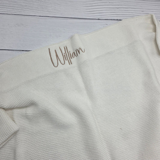 Light gray fabric with 'William' embroidered on a wooden surface