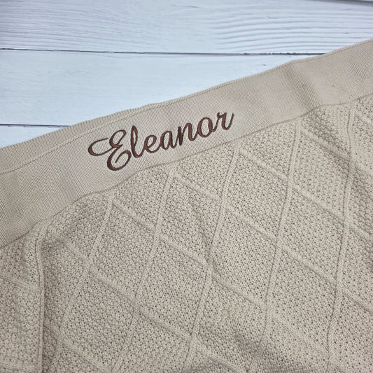 Textured beige fabric with embroidered name 'Eleanor' on a light wooden surface