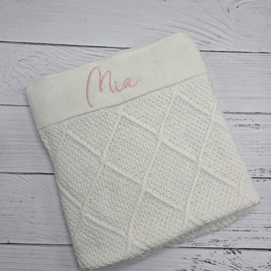 Textured blanket with 'Mia' embroidery on a wooden surface