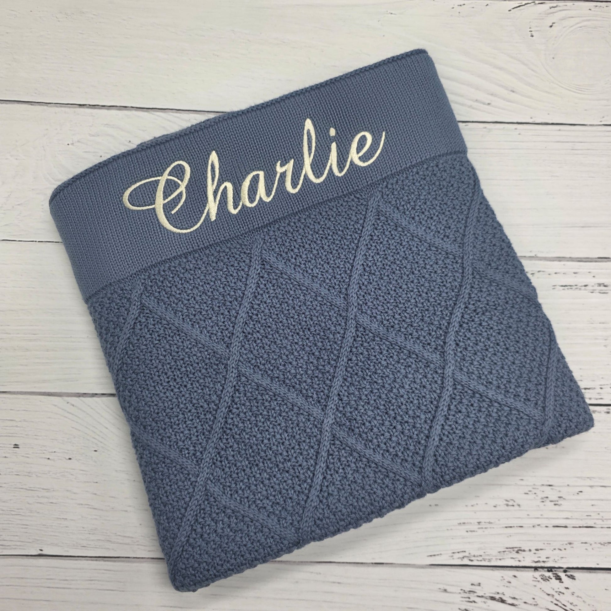 Blue knitted blanket with 'Charlie' embroidered on a wooden surface