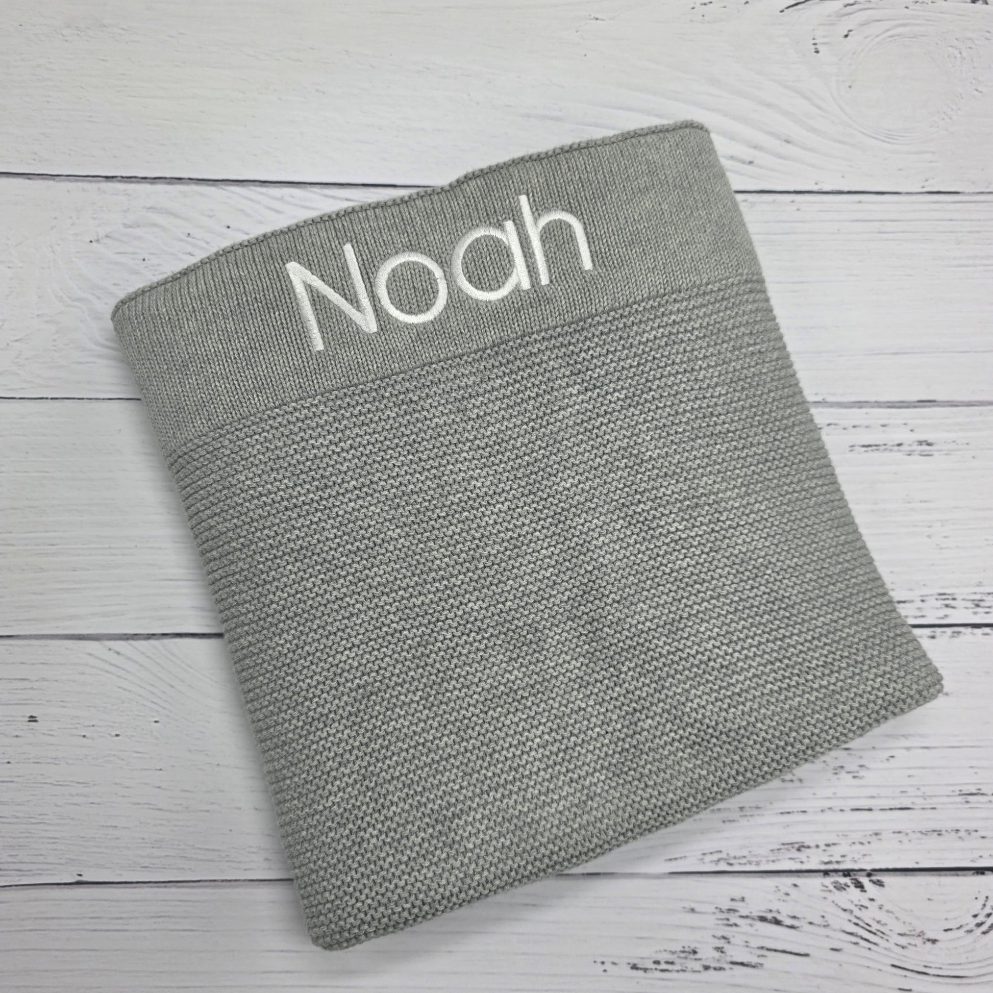 Gray textured blanket with 'Noah' embroidered on a wooden surface
