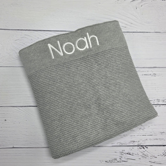Gray textured blanket with 'Noah' embroidered on a wooden surface