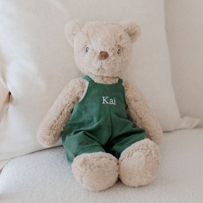 Stuffed teddy bear wearing a green outfit with 'Kai' on it, sitting on a white couch.
