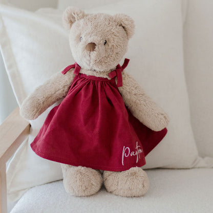 Teddy bear in a red dress sitting on a white cushion
