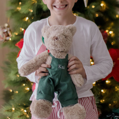 Child holding a teddy bear in front of a decorated Christmas tree