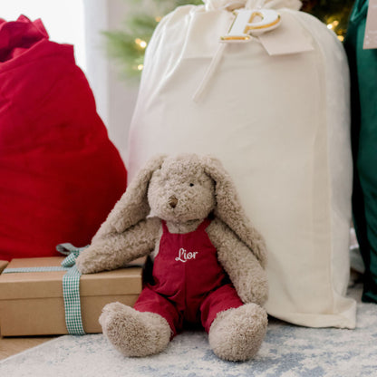 nana huchy bunny animal in a personalised red outfit sitting next to a Christmas tree and wrapped gifts.