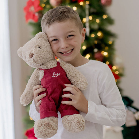 Child holding a teddy bear in front of a decorated Christmas tree