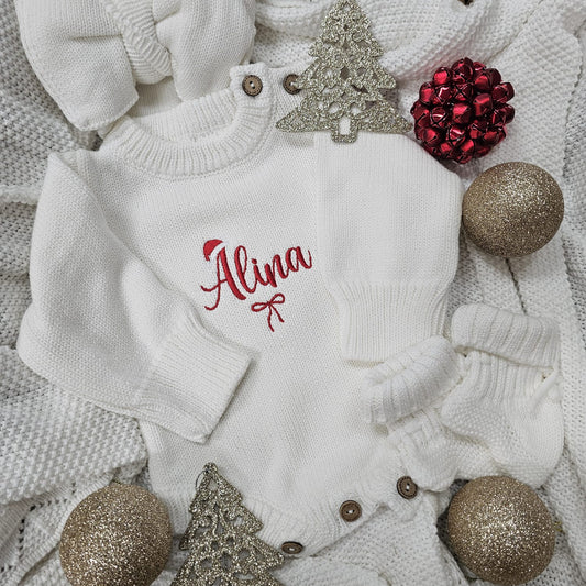 White baby outfit with 'Alina' embroidered on it, surrounded by Christmas decorations.