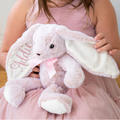 Young girl holding a pink bunny plush toy in a softly lit room.