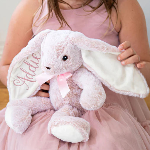 Young girl holding a pink bunny plush toy in a softly lit room.